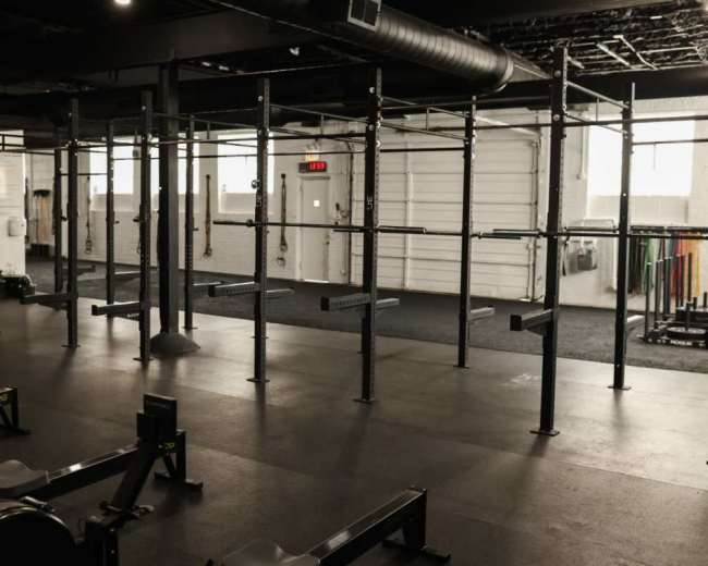 The image shows a spacious gym with various exercise equipment, including rowing machines, and a set of parallel bars or pull-up bars in an open area.