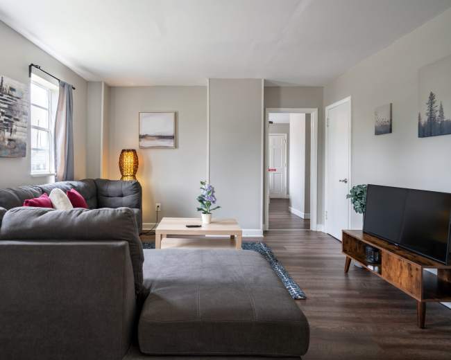 The image shows a modern living room with a gray sectional sofa, a coffee table, a television, and artwork on the walls.