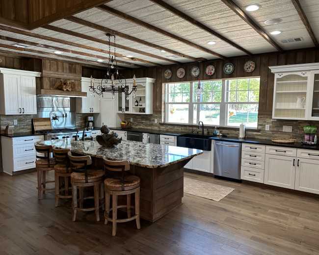 The kitchen features wooden beams on the ceiling, a large island with seating, white cabinetry, and an array of stainless steel appliances.