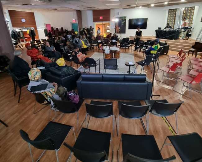 The image shows a spacious indoor gathering area with circular seating arrangements, including chairs and couches, set up for an event.