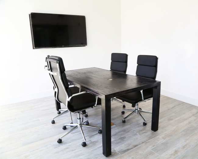 A modern meeting room features a black table surrounded by four ergonomic chairs, with a large TV mounted on the wall.