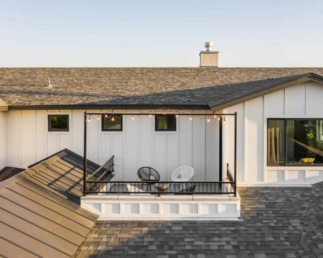 The image shows an aerial view of a house with a deck featuring two chairs and string lights, surrounded by sloped roofs.