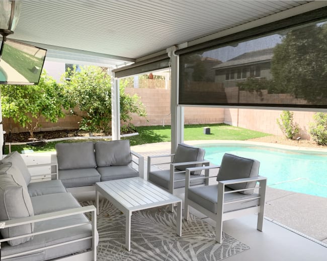 The image showcases a covered patio area with outdoor furniture overlooking a pool and landscaped yard.