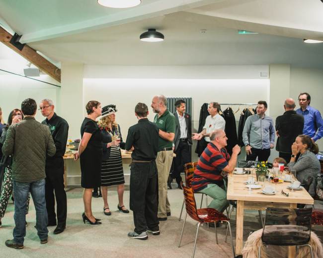 A group of people are mingling and dining in a spacious indoor area with tables and seating arrangements.