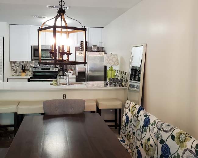 A dining area with a wooden table, a patterned sofa, and an attached kitchen featuring white cabinets and stainless steel appliances.