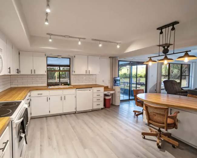 A clean kitchen features white cabinets, a wooden countertop, and large windows that provide natural light.