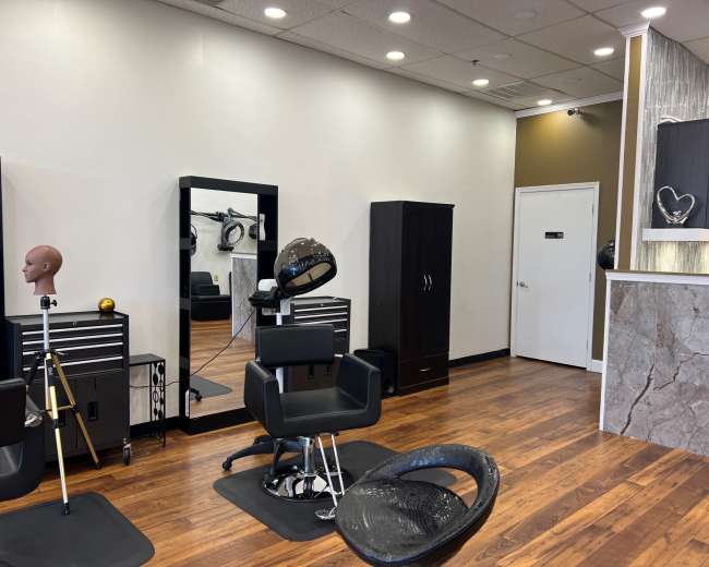 A well-lit hair salon interior featuring styling chairs, a mirror, and storage cabinets against wooden flooring.