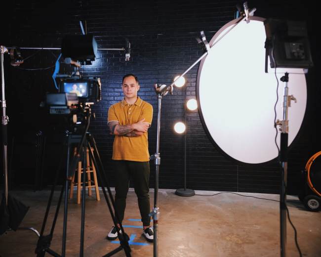 A man stands in a photo studio surrounded by cameras and lighting equipment.