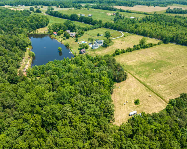The image shows a rural landscape featuring a small pond surrounded by trees, with several fields and homes in the distance.