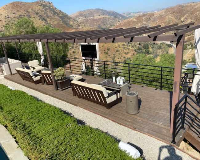 A wooden deck with lounge seating and a flat-screen TV overlooks a hilly landscape.