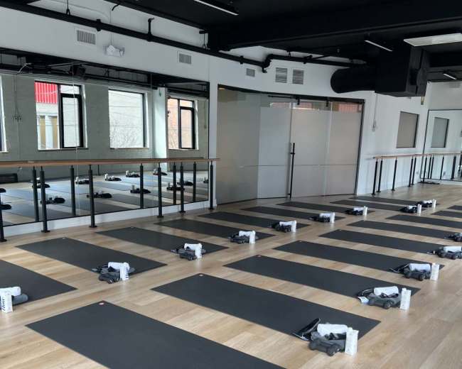 The image shows a yoga studio with neatly arranged mats and water bottles set up for a class.