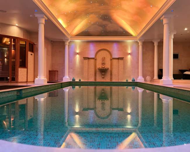 The image shows a luxurious indoor pool area with a decorative ceiling and ambient lighting.
