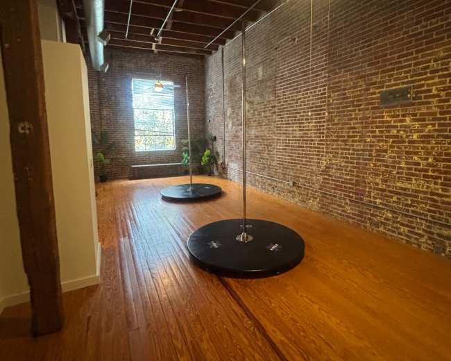 The image shows a spacious, well-lit room with two black circular platforms and exposed brick walls.