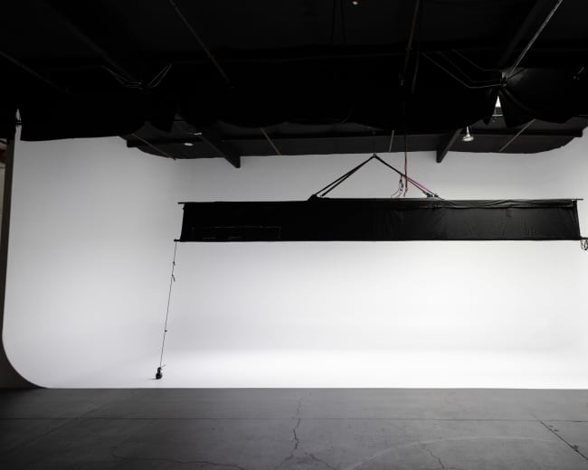 The image shows a spacious photography studio with a seamless white backdrop and a large overhead light fixture.