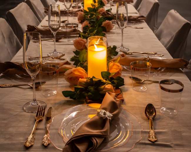 A long dining table is set for a formal event with elegant tableware, candles, and floral decorations.