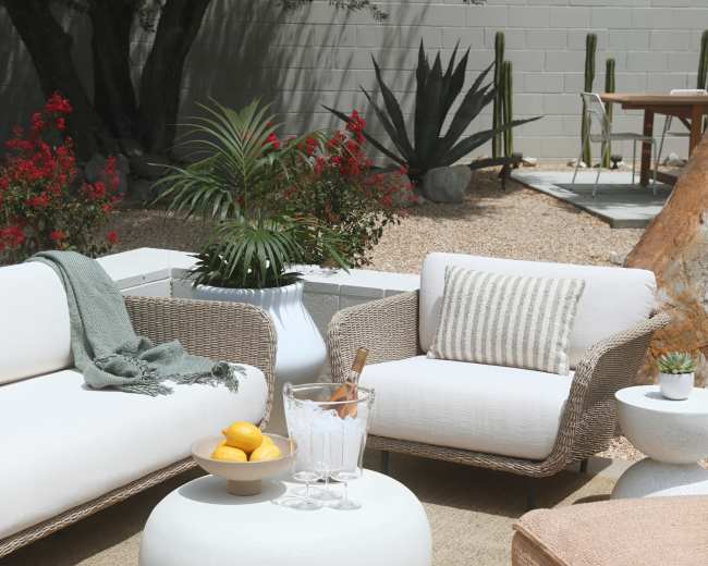 A cozy outdoor seating area features two couches, a round coffee table, and decorative elements like a plant and a bowl of lemons.