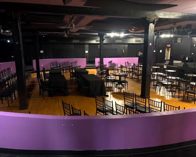 The image shows a large event space with rows of empty chairs and tables, featuring a purple and black color scheme.