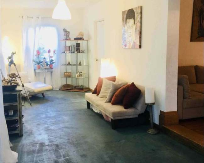 The image shows a living space with a light-colored sofa, decorative shelves, and a mix of seating arrangements under a neutral-colored light fixture.