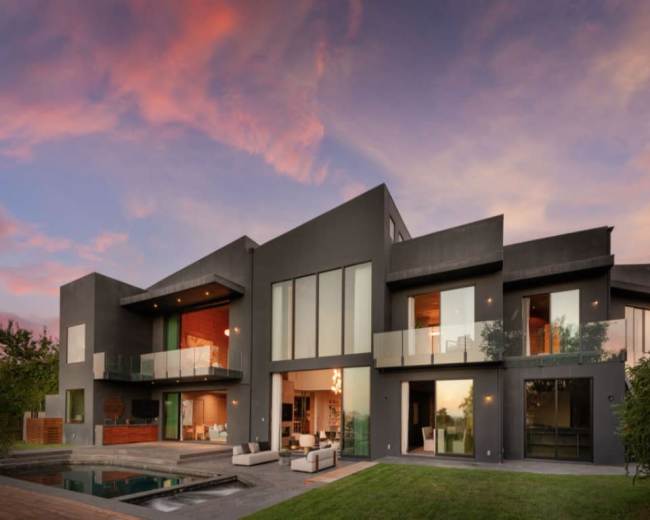 A modern two-story house features large glass windows and a backyard pool under a colorful sky.
