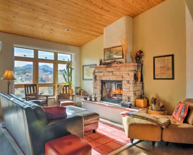 The room features a stone fireplace as the centerpiece, surrounded by seating and large windows that overlook a desert landscape.