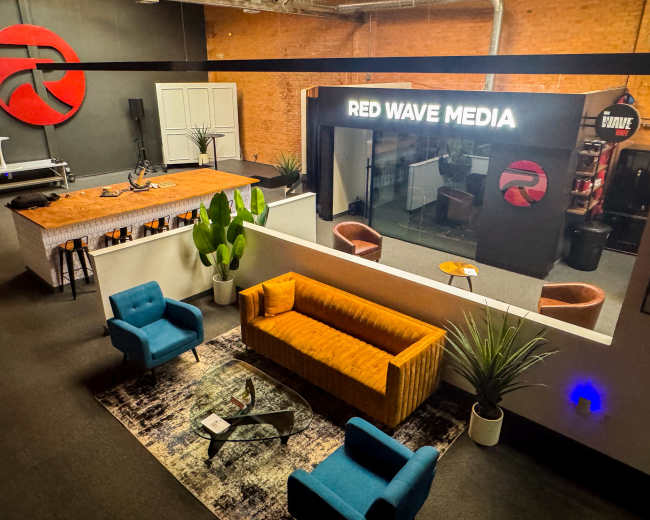 The image shows a modern office space with a reception area featuring a large logo, a bar-like seating area, and colorful furniture, including a blue chair and a yellow sofa.