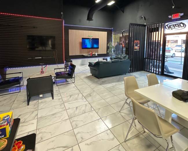 The image shows a modern lounge area with black walls, a large TV, and seating, along with a table and children's toys on the tiled floor.