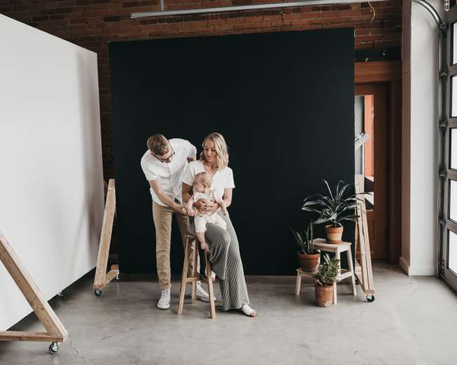 A family poses for a photo session in a studio with contrasting backdrops and potted plants.
