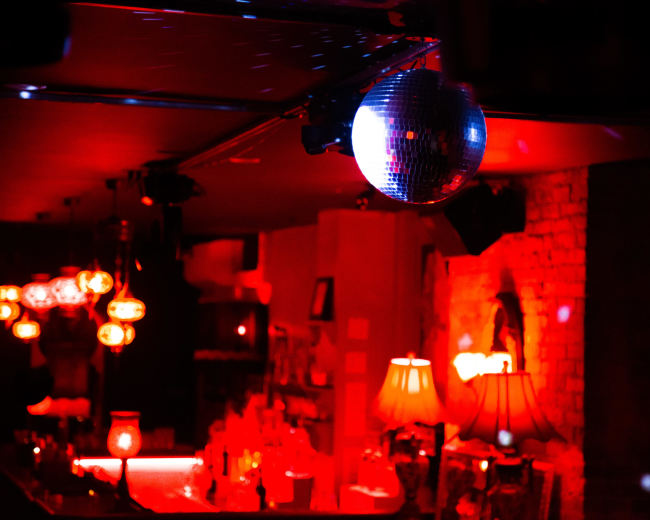 A disco ball hangs above a bar illuminated by red and soft amber lighting.