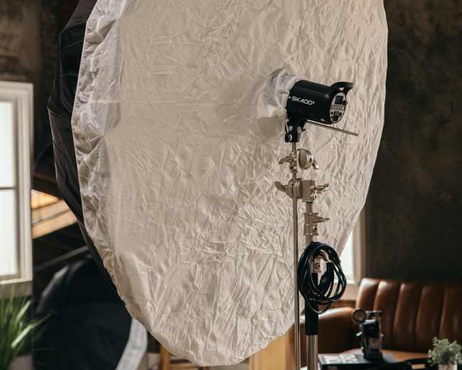 A large, circular softbox is positioned on a stand in a room with wooden floors and a brown leather couch.