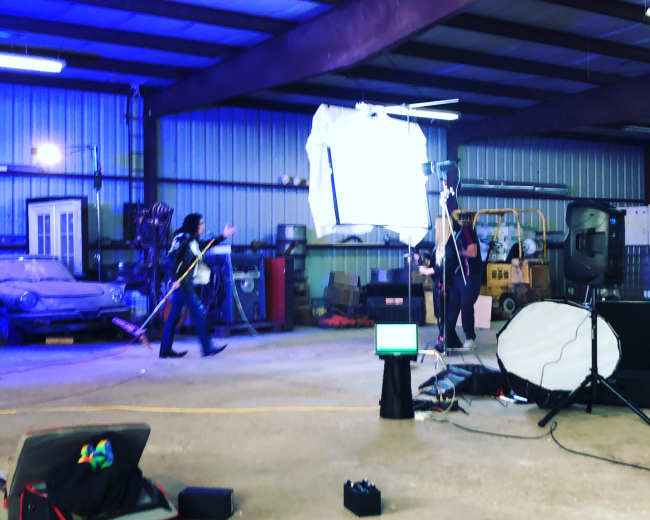 A band performs in a large industrial space, with musical equipment set up and stage lights illuminating the area.