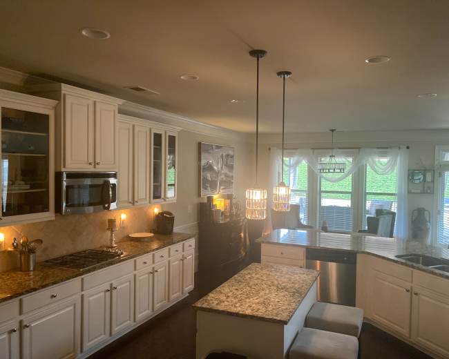 The image shows a modern kitchen with white cabinetry, granite countertops, and a central island with pendant lighting.