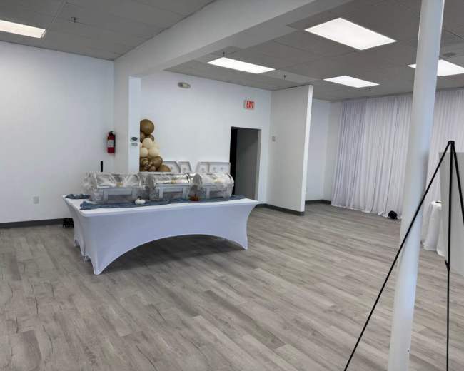The image shows an event space with a buffet setup on a table covered with a white tablecloth and balloons in the background.