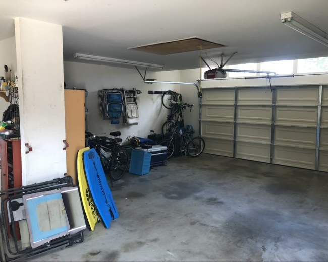 A garage with bicycles hanging on the wall, a blue storage container, and various tools scattered on the floor.
