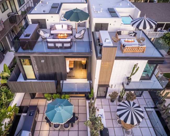 A modern multi-level residence with various outdoor seating areas, including a rooftop terrace and a patio surrounded by greenery.