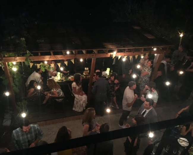 A large gathering of people socializing under string lights in a wooden structure with festive decorations.