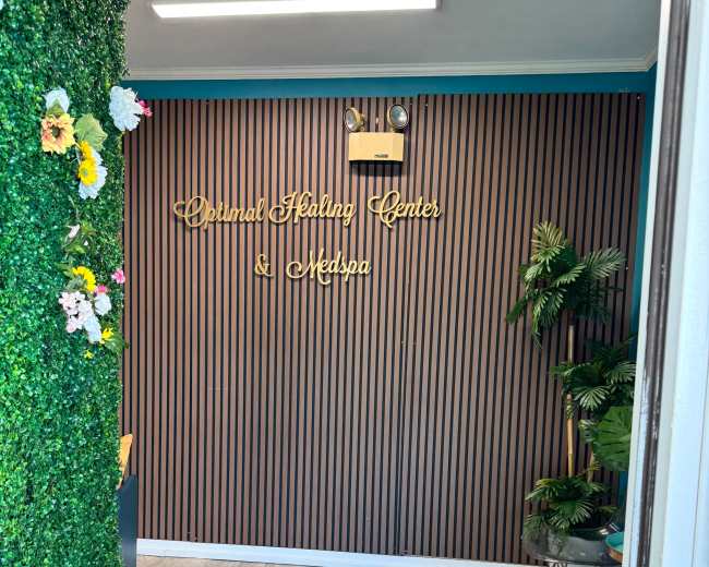The image shows the interior of a wellness center with a wall featuring vertical stripes and decorative greenery, including flowers, alongside the sign for "Dermal Healing Center & Medspa."
