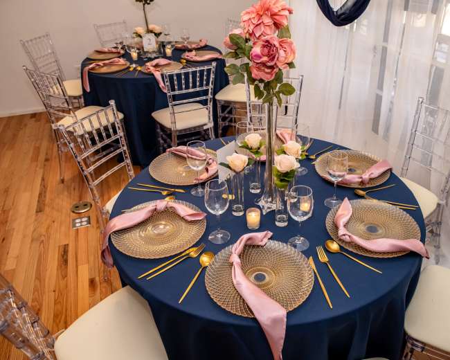 Elegantly arranged dining tables with navy tablecloths, charger plates, and floral centerpieces.