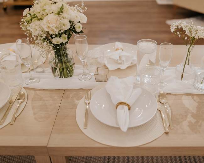 A neatly arranged dining table is set with white plates, glassware, and small floral centerpieces.