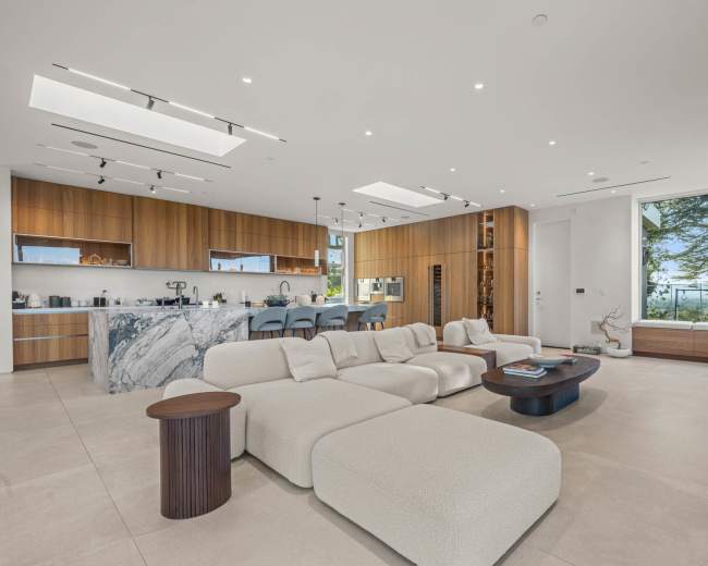 The spacious living area features a large, U-shaped sofa, a wooden coffee table, and a modern kitchen with a marble island and wooden cabinetry.