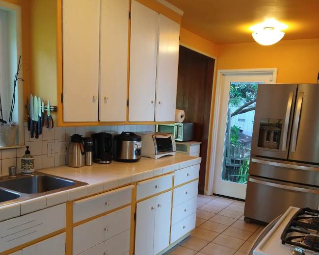The kitchen features white cabinets with yellow trim, a tiled floor, and stainless steel appliances, including a refrigerator and stove.