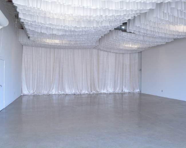 A spacious, empty room with a polished concrete floor and draped white fabric installations on the ceiling.
