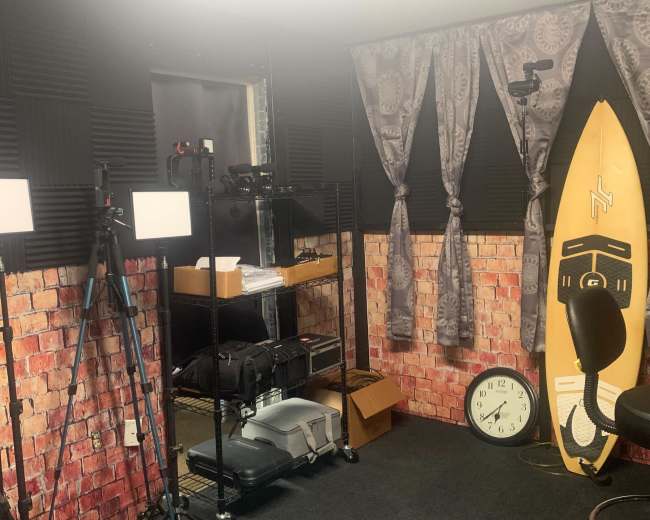 A small recording studio with soundproof walls, lighting equipment, a surfboard, and a wall clock.