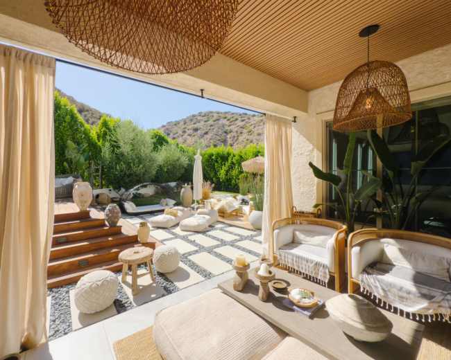 A stylish outdoor living space features a comfortable seating area with woven decor, surrounded by lush greenery and stone pathways.