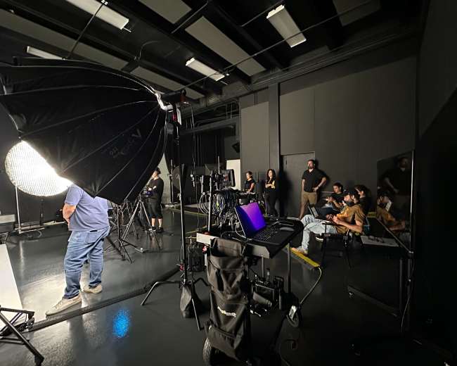 A photography studio setup features multiple lighting equipment and a group of people seated in front of a screen.