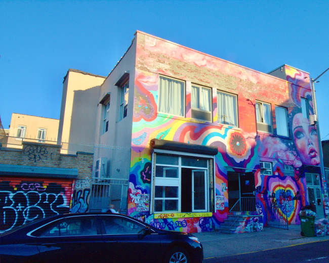 A multi-story building features a vibrant mural on its facade, showcasing colorful abstract designs and portraits.