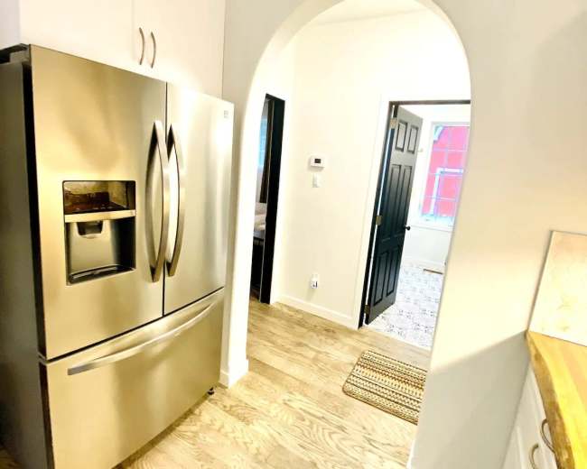 The image shows a kitchen area with a stainless steel refrigerator on the left and an arched doorway leading to another room on the right.