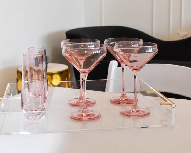 A set of pink glassware is arranged on a tray beside a black chair and a decorative drum.