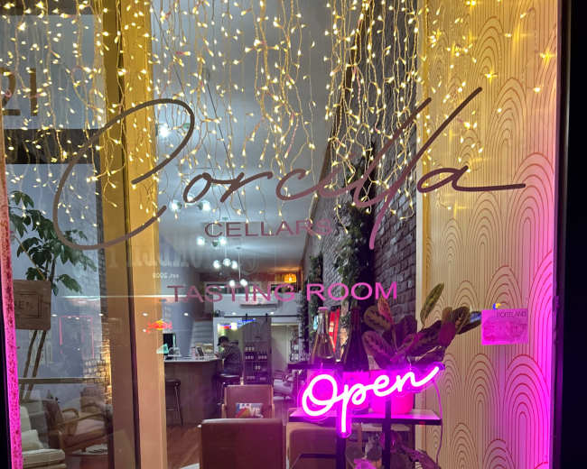 The window display features a neon "Open" sign, adorned with decorative plants and a bottle of wine, inviting customers into a tasting room.