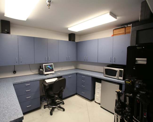 A small, organized office space features blue cabinets, a desk with a computer, and appliances like a microwave and a mini-fridge.