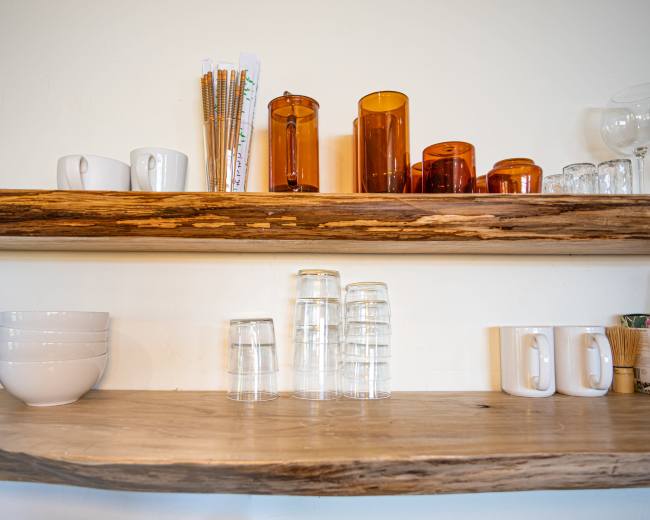 The image shows two wooden shelves displaying a variety of glassware, mugs, and bowls organized neatly.